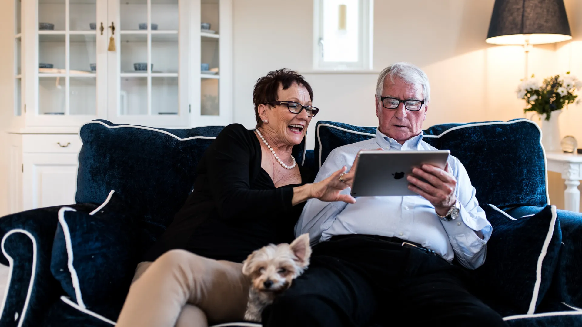 A man and a woman sat on a sofa using a iPad