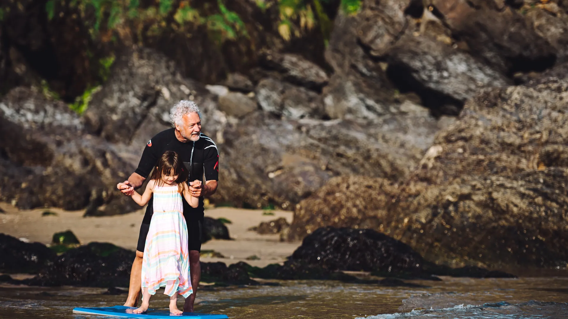 A grandad and granddaughter paddle-boarding in the sea in Devon