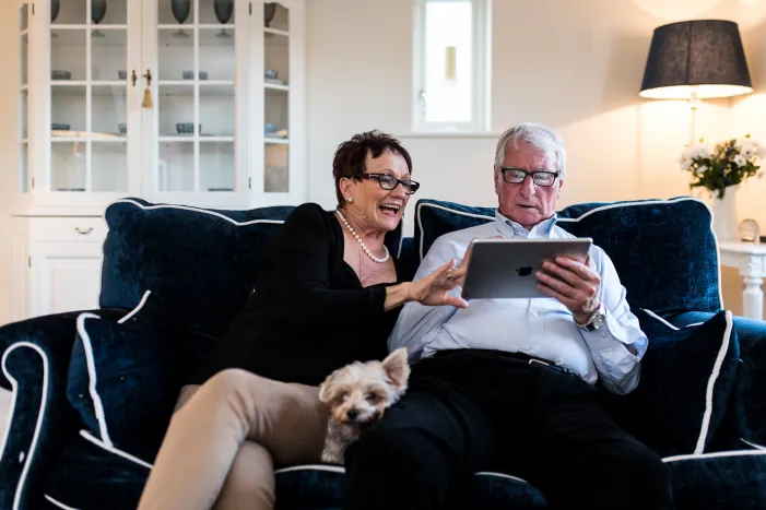 A man and a woman sat on a sofa using a iPad