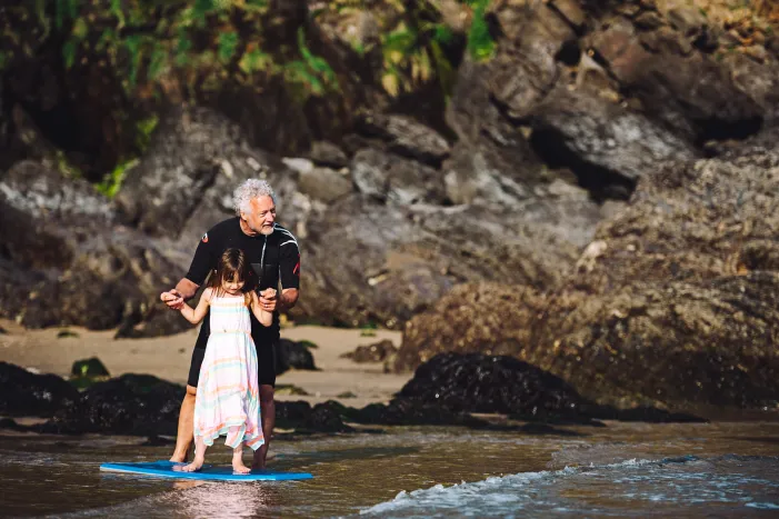 A grandad and granddaughter paddle-boarding in the sea in Devon
